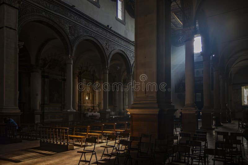 June 4, 2023 - Ferrara. The dark and silent interior of an ancient church. Light filtering through the rose window, illuminating the chairs and benches. A solitary believer is absorbed in prayer. June 4, 2023 - Ferrara. The dark and silent interior of an ancient church. Light filtering through the rose window, illuminating the chairs and benches. A solitary believer is absorbed in prayer