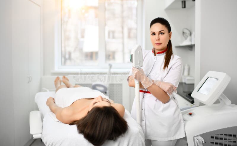 l'Medico-estetista in abito bianco con un apparecchio medico è pronto ad eseguire un procedur cosmetico per un paziente nel salon fotografie stock l'Medico-estetista in abito bianco con un apparecchio medico è pronto ad eseguire un procedur cosmetico per un paziente nel salon fotografie stock