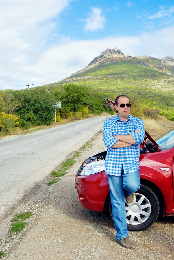 L'uomo adulto sta stando vicino alla sua automobile rotta fotografie stock L'uomo adulto sta stando vicino alla sua automobile rotta fotografie stock