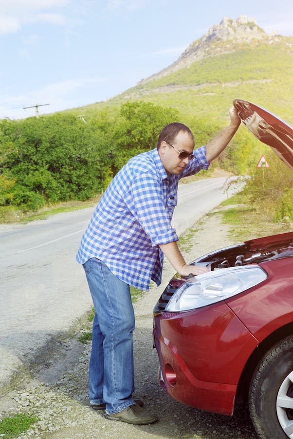 L'uomo adulto sta stando vicino alla sua automobile rotta immagini stock libere da diritti L'uomo adulto sta stando vicino alla sua automobile rotta immagini stock libere da diritti