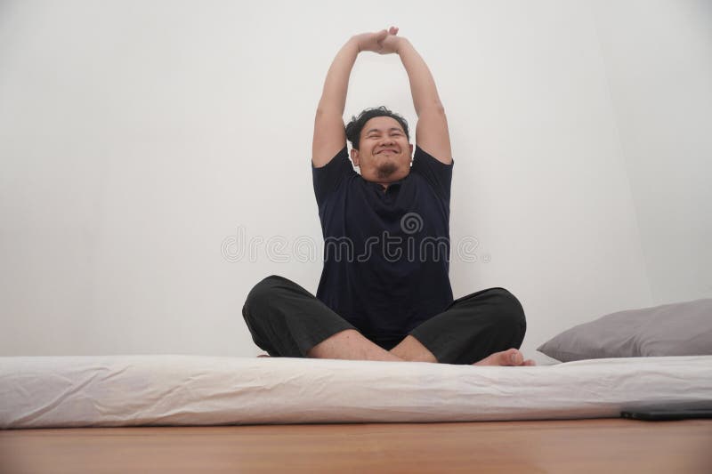 L'uomo asiatico che si stende sul materasso nella camera del letto fa esercizio dopo essersi svegliato la mattina immagine stock