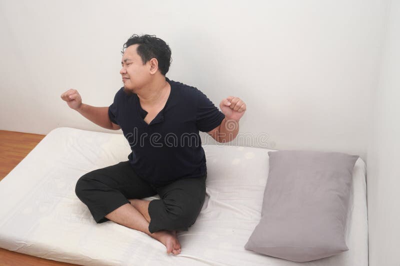 L'uomo asiatico che si stende sul materasso nella camera del letto fa esercizio dopo essersi svegliato la mattina fotografie stock