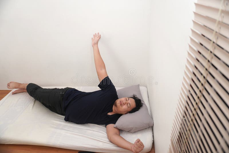 L'uomo asiatico che si stende sul materasso nella camera del letto fa esercizio dopo essersi svegliato la mattina immagine stock libera da diritti