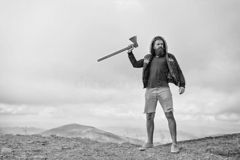 L'uomo barbuto, pantaloni a vita bassa brutali con i baffi tiene l'ascia sulla montagna immagine stock libera da diritti L'uomo barbuto, pantaloni a vita bassa brutali con i baffi tiene l'ascia sulla montagna immagine stock libera da diritti