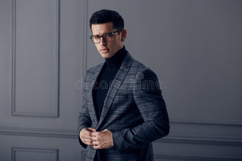 L'uomo bello e adatto in vestito grigio con il collo alto nero, occhiali alla moda neri esamina sicuro la macchina fotografica immagine stock L'uomo bello e adatto in vestito grigio con il collo alto nero, occhiali alla moda neri esamina sicuro la macchina fotografica immagine stock