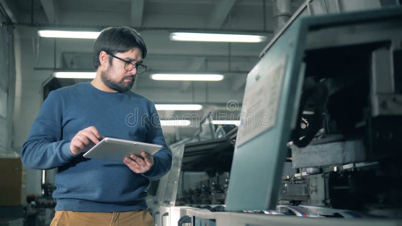 L'uomo con un computer della compressa sta ispezionando le apparecchiature di stampa di funzionamento