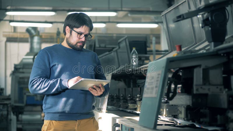 L'uomo controlla il lavoro del trasportatore tipografico, scrivente su una compressa