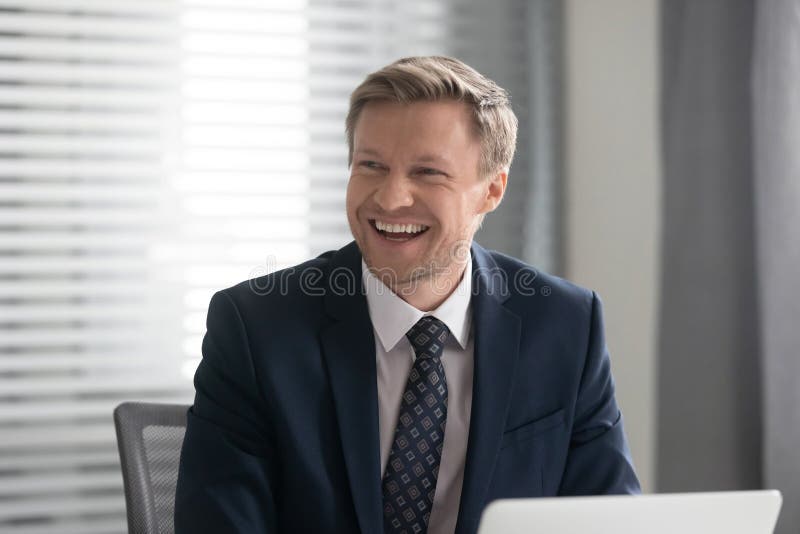 L'uomo d'affari allegro felice nella risata del vestito si siede allo scrittorio del lavoro fotografia stock libera da diritti