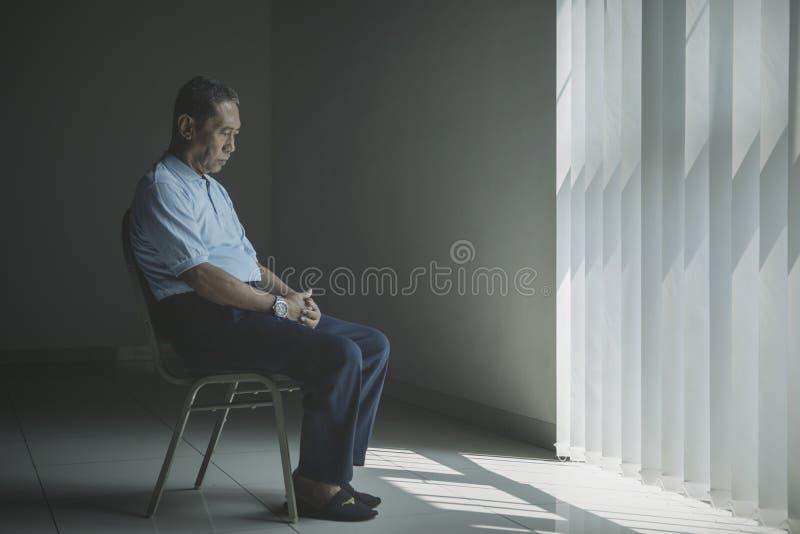 L'uomo invecchiato solo sembra triste vicino alla finestra fotografie stock L'uomo invecchiato solo sembra triste vicino alla finestra fotografie stock