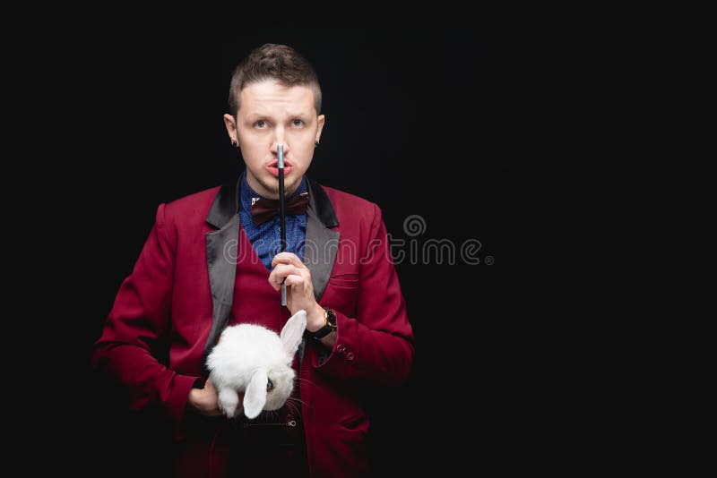 L'uomo mago fa il trucco con un coniglio bianco e una bacchetta magica copia lo sfondo nero dello spazio immagine stock