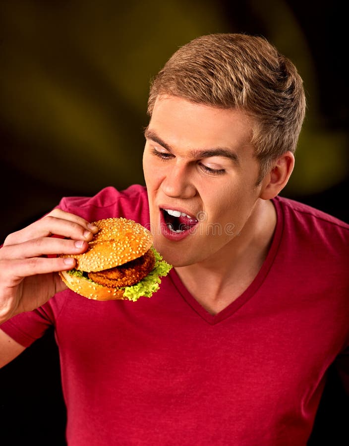 L'uomo mangia l'hamburger Concetto degli alimenti industriali e di pasto rapido