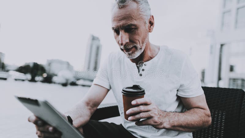 L'uomo sta utilizzando un PC della compressa e sta bevendo un caffè fotografia stock libera da diritti L'uomo sta utilizzando un PC della compressa e sta bevendo un caffè fotografia stock libera da diritti