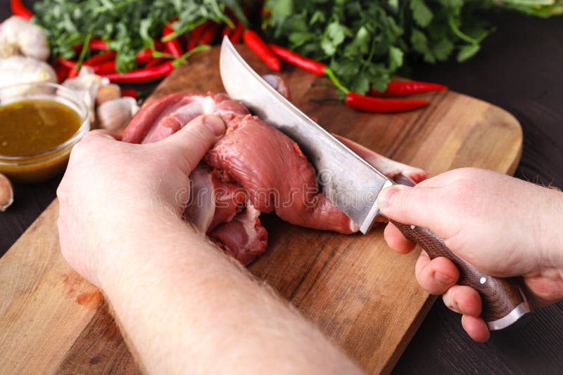 L'uomo taglia la carne fresca a pezzi per il barbecue immagine stock L'uomo taglia la carne fresca a pezzi per il barbecue immagine stock