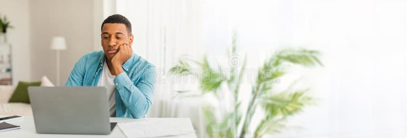 Young african american man shows boredom as he works on his laptop, with plenty of copy space on the left for web-banner purposes. Young african american man shows boredom as he works on his laptop, with plenty of copy space on the left for web-banner purposes