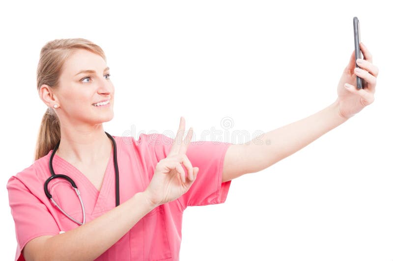 Nurse wearing scrubs taking selfie with smartphone showing peace and smiling isolated on white background. Nurse wearing scrubs taking selfie with smartphone showing peace and smiling isolated on white background