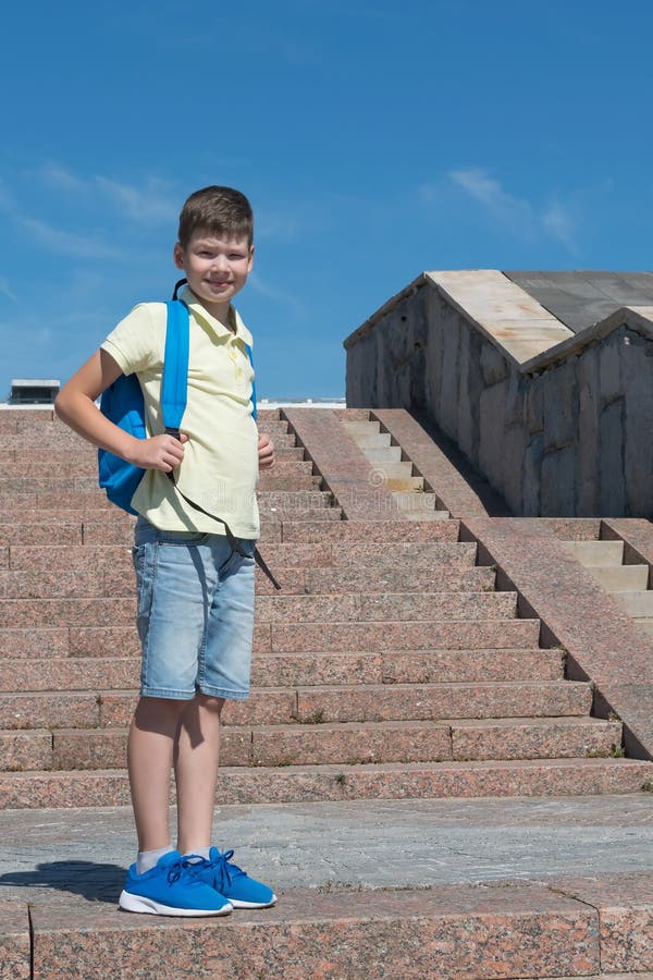 L'écolier se tient sur les escaliers avec un sac à dos bleu pour l'école image libre de droits L'écolier se tient sur les escaliers avec un sac à dos bleu pour l'école image libre de droits