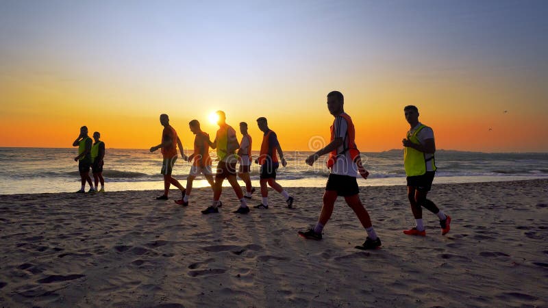 L'équipe de football, donnant des leçons particulières au fonctionnement de formation extérieur sous le coucher du soleil de plag photos stock L'équipe de football, donnant des leçons particulières au fonctionnement de formation extérieur sous le coucher du soleil de plag photos stock