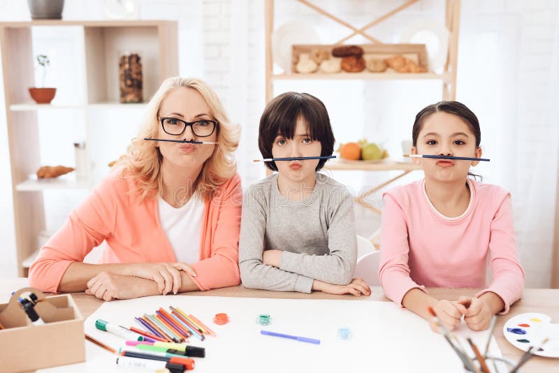La abuela joven, junto con sus nietos, hace caras con la ayuda de cepillos imagen de archivo libre de regalías La abuela joven, junto con sus nietos, hace caras con la ayuda de cepillos imagen de archivo libre de regalías