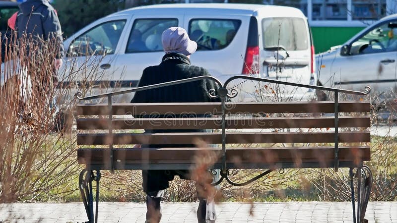 La abuela se sienta en un banco en un parque de la mujer mayor