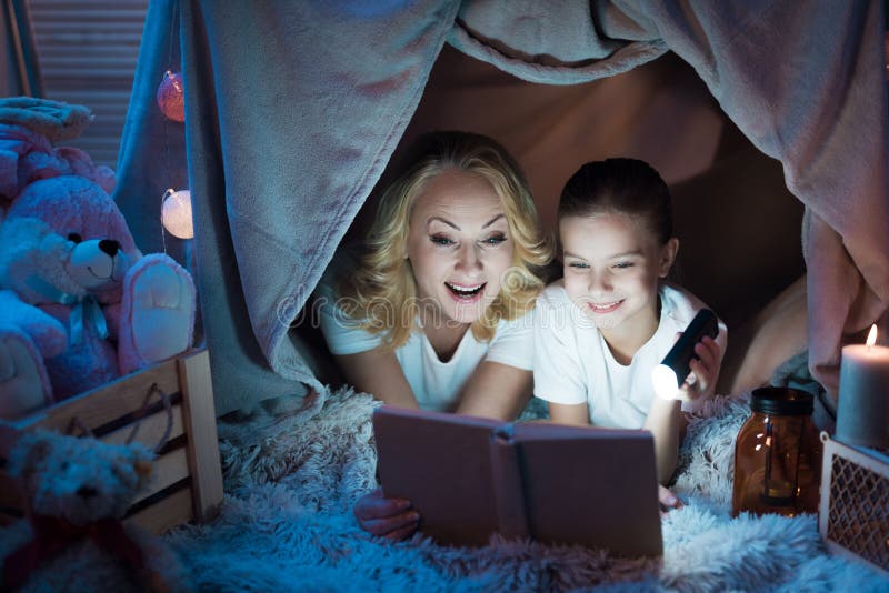La abuela y la nieta están leyendo cuentos de hadas en la casa combinada en la noche en casa foto de archivo La abuela y la nieta están leyendo cuentos de hadas en la casa combinada en la noche en casa foto de archivo
