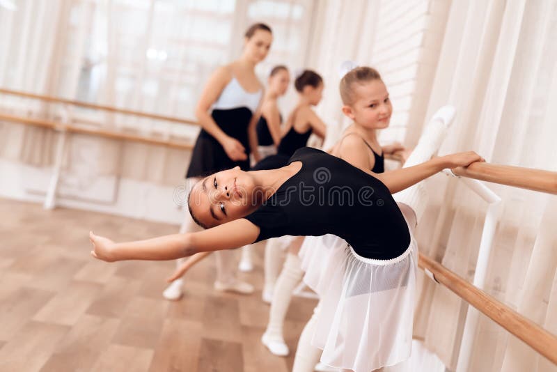 The young ballerina makes a dance movement with her hands during a class at a ballet school. The trainer of the ballet school helps young ballerinas perform different choreographic exercises. The young ballerina makes a dance movement with her hands during a class at a ballet school. The trainer of the ballet school helps young ballerinas perform different choreographic exercises.