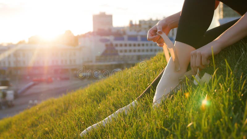La ballerine attache ses chaussures de pointe se reposant sur l'herbe verte sur la colline photographie stock libre de droits La ballerine attache ses chaussures de pointe se reposant sur l'herbe verte sur la colline photographie stock libre de droits