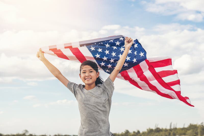 La bambina asiatica felice con la bandiera americana U.S.A. celebra il quarto luglio immagini stock La bambina asiatica felice con la bandiera americana U.S.A. celebra il quarto luglio immagini stock