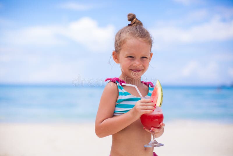La bambina beve il succo dall'anguria sul fotografia stock La bambina beve il succo dall'anguria sul fotografia stock