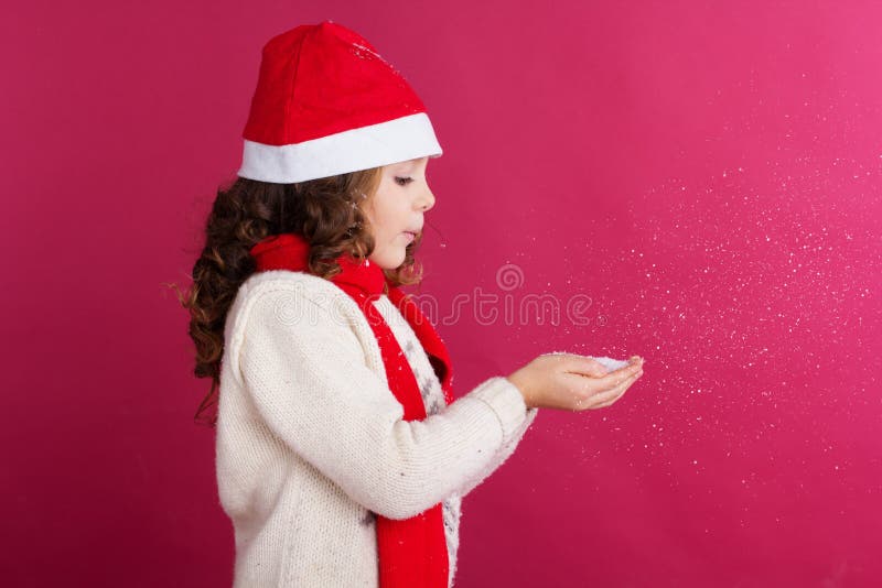 La bambina in cappello di Santa sta tenendo la neve falsa fotografie stock La bambina in cappello di Santa sta tenendo la neve falsa fotografie stock