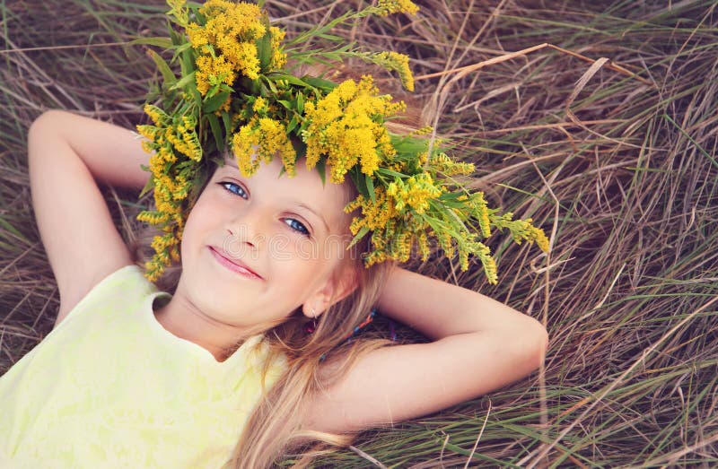 La bambina felice in fiori corona mettere sull'erba fotografia stock La bambina felice in fiori corona mettere sull'erba fotografia stock