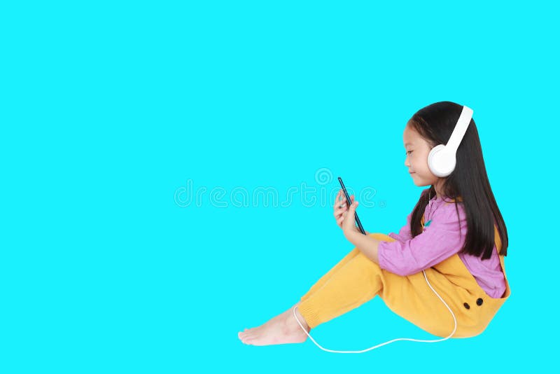 La bambina felice gode di di ascoltare la musica con le cuffie isolate su ciano fondo con lo spazio della copia fotografia stock libera da diritti La bambina felice gode di di ascoltare la musica con le cuffie isolate su ciano fondo con lo spazio della copia fotografia stock libera da diritti