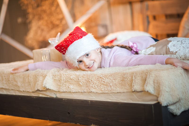 La bambina nel cappuccio di Santa Claus sta aspettando il nuovo anno sul letto Ragazza sul Natale con i regali nella camera da le fotografie stock La bambina nel cappuccio di Santa Claus sta aspettando il nuovo anno sul letto Ragazza sul Natale con i regali nella camera da le fotografie stock