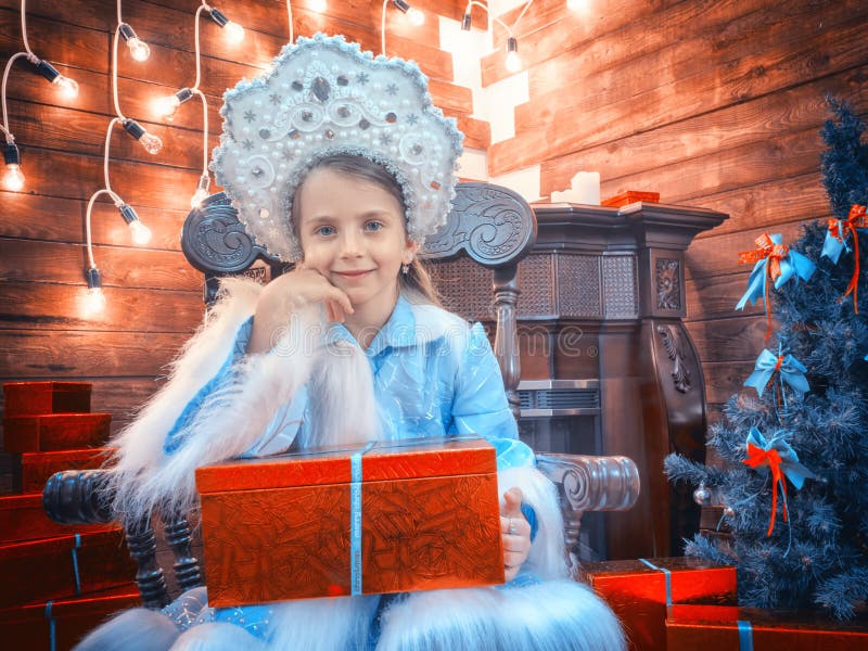 La bambina piacevole ha peso i gomiti su una scatola con i regali ed i sorrisi immagini stock libere da diritti La bambina piacevole ha peso i gomiti su una scatola con i regali ed i sorrisi immagini stock libere da diritti
