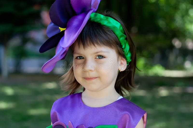 La bambina in un vestito del fiore viola sta sorridendo fotografia stock La bambina in un vestito del fiore viola sta sorridendo fotografia stock