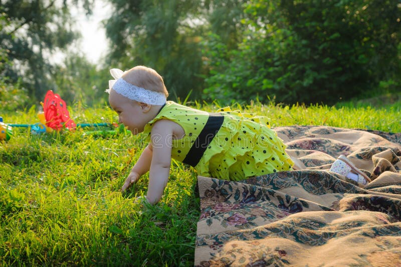 La bambina in un vestito giallo striscia su un'erba verde immagine stock La bambina in un vestito giallo striscia su un'erba verde immagine stock