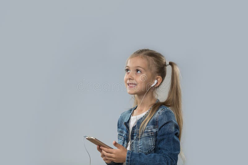 La bella bambina che per mezzo dello Smart Phone ascolta sguardo sorridente felice delle cuffie di usura di musica per copiare lo immagini stock La bella bambina che per mezzo dello Smart Phone ascolta sguardo sorridente felice delle cuffie di usura di musica per copiare lo immagini stock