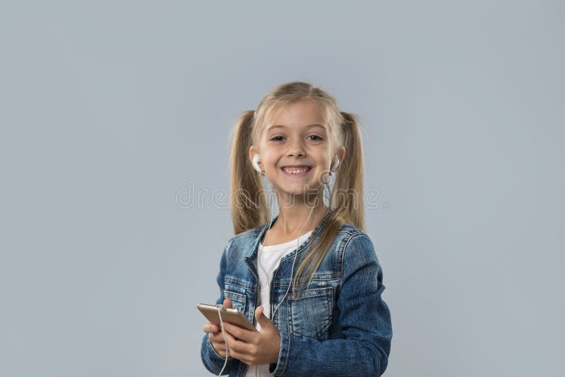 La bella bambina che per mezzo dello Smart Phone delle cellule ascolta sorridere felice delle cuffie di usura di musica isolato fotografia stock La bella bambina che per mezzo dello Smart Phone delle cellule ascolta sorridere felice delle cuffie di usura di musica isolato fotografia stock