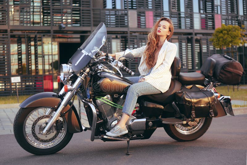 La bella bionda si siede su un motociclo vicino all'ufficio La ragazza è venuto a lavorare ad un motociclo Successo La ragazza si immagine stock La bella bionda si siede su un motociclo vicino all'ufficio La ragazza è venuto a lavorare ad un motociclo Successo La ragazza si immagine stock