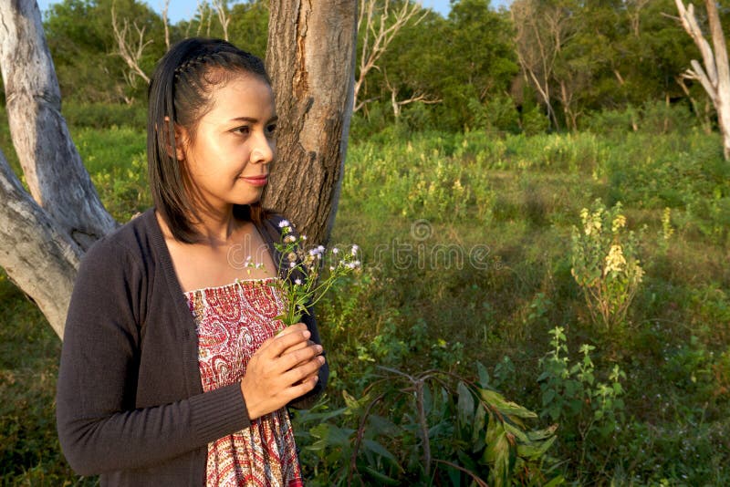 La bella donna asiatica è sorridente e tenente un gruppo di fiori selvaggi minuscoli in sua mano fotografia stock libera da diritti La bella donna asiatica è sorridente e tenente un gruppo di fiori selvaggi minuscoli in sua mano fotografia stock libera da diritti