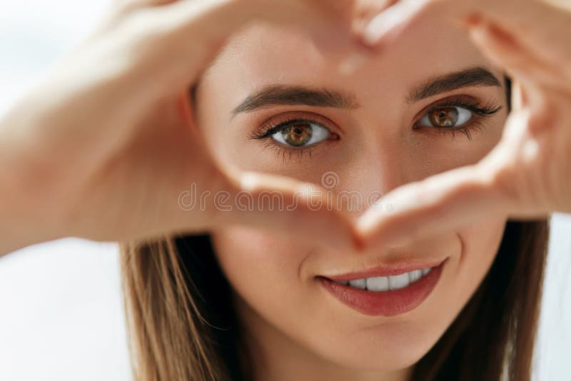 La bella donna felice che mostra il segno di amore vicino osserva fotografia stock