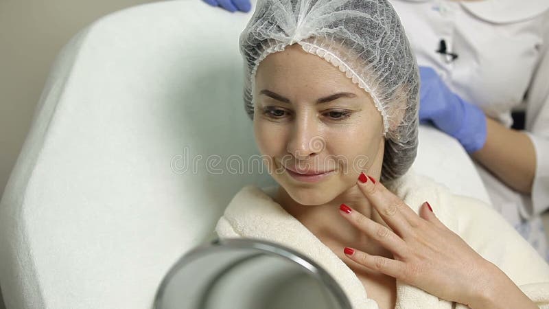 La bella donna la esamina in specchio dopo le procedure cosmetiche nel salone di bellezza