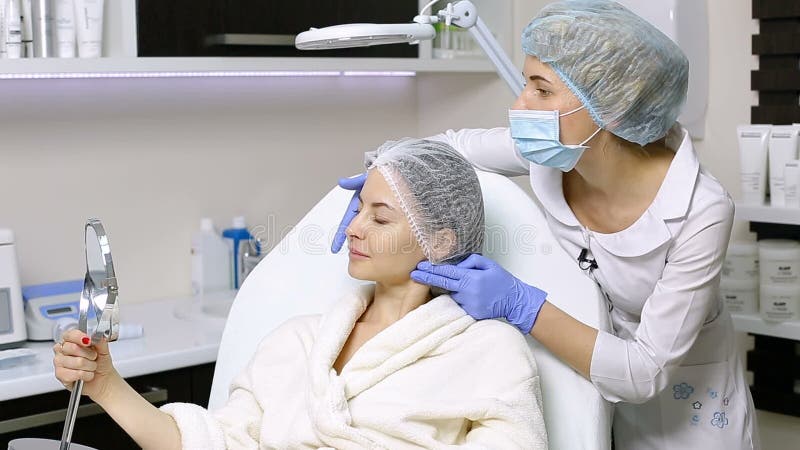 La bella donna la esamina in specchio dopo le procedure cosmetiche nel salone di bellezza