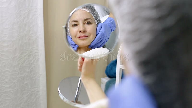 La bella donna la esamina in specchio dopo le procedure cosmetiche nel salone di bellezza