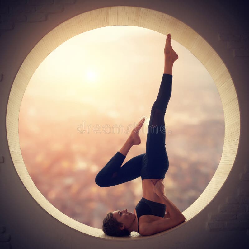 La bella donna sportiva degli Yogi di misura pratica l'yoga Salamba Sarvangasana - posa dello shoulderstand in una finestra La bella donna sportiva degli Yogi di misura pratica l'yoga Salamba Sarvangasana - posa dello shoulderstand in una finestra