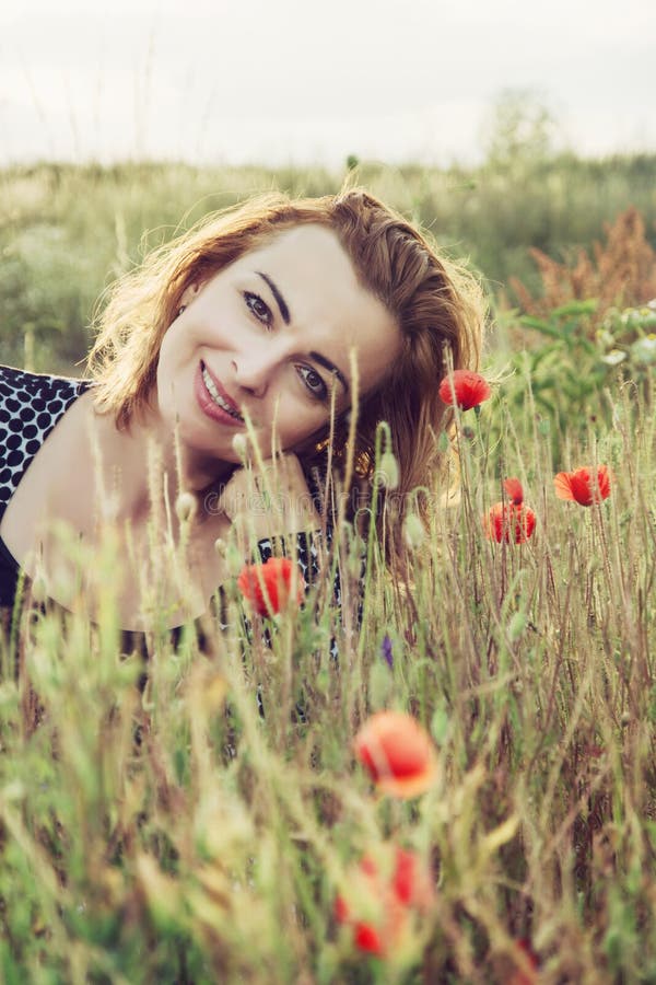 La bella donna è sorridente e posante nel giacimento di fiori del papavero immagini stock La bella donna è sorridente e posante nel giacimento di fiori del papavero immagini stock