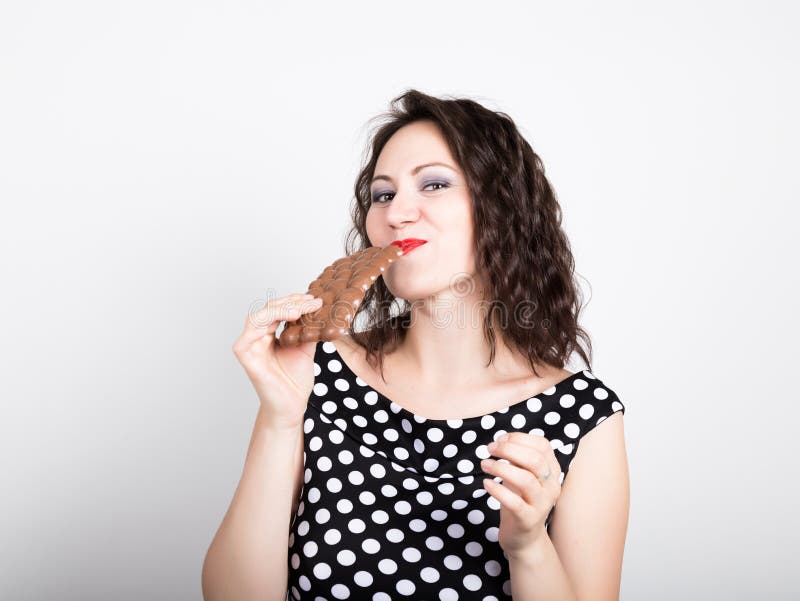 La bella giovane donna che mangia una barra di cioccolato, porta un vestito con i pois fotografia stock libera da diritti La bella giovane donna che mangia una barra di cioccolato, porta un vestito con i pois fotografia stock libera da diritti
