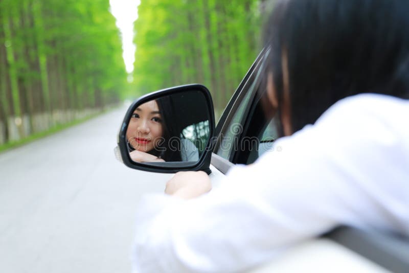 La bella giovane donna cinese asiatica felice si siede su uno sguardo bianco dell'automobile a se stessa dal retrovisore dell'aut fotografie stock libere da diritti La bella giovane donna cinese asiatica felice si siede su uno sguardo bianco dell'automobile a se stessa dal retrovisore dell'aut fotografie stock libere da diritti