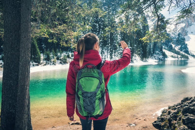 La bella giovane donna con lo zaino sta facendo il selfie sul lago immagine stock libera da diritti La bella giovane donna con lo zaino sta facendo il selfie sul lago immagine stock libera da diritti