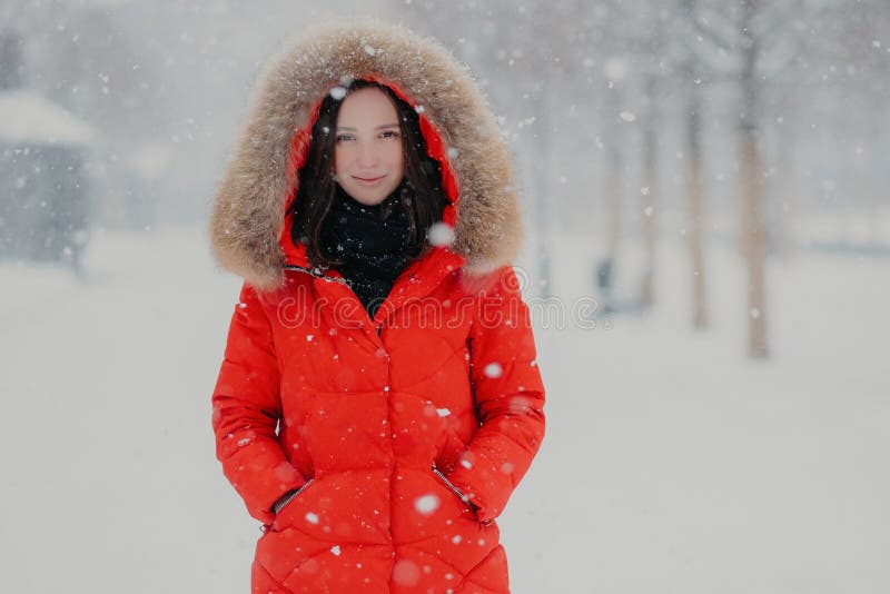 La bella giovane donna ha appello dello sguardo, porta il rivestimento rosso caldo, tiene le mani in tasche, ha passeggiata all'a immagini stock La bella giovane donna ha appello dello sguardo, porta il rivestimento rosso caldo, tiene le mani in tasche, ha passeggiata all'a immagini stock