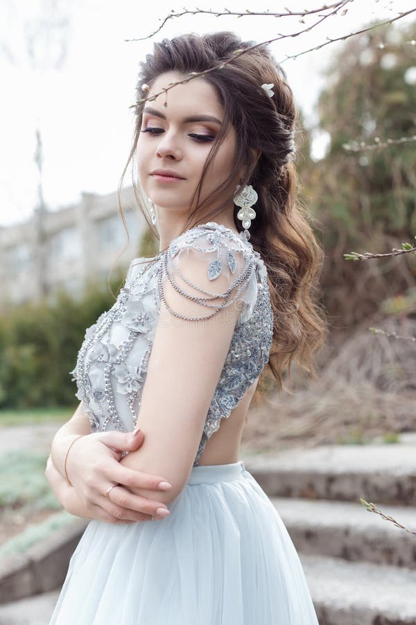 La bella giovane ragazza gay tenera con la bella acconciatura di nozze con un sorriso bianco come la neve in vestito leggero sta fotografia stock libera da diritti La bella giovane ragazza gay tenera con la bella acconciatura di nozze con un sorriso bianco come la neve in vestito leggero sta fotografia stock libera da diritti